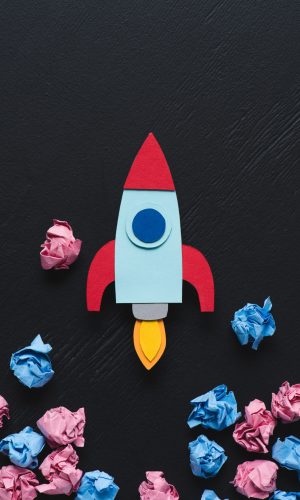 cardboard rocket with pink and blue crumpled paper balls on black background, setting goals concept